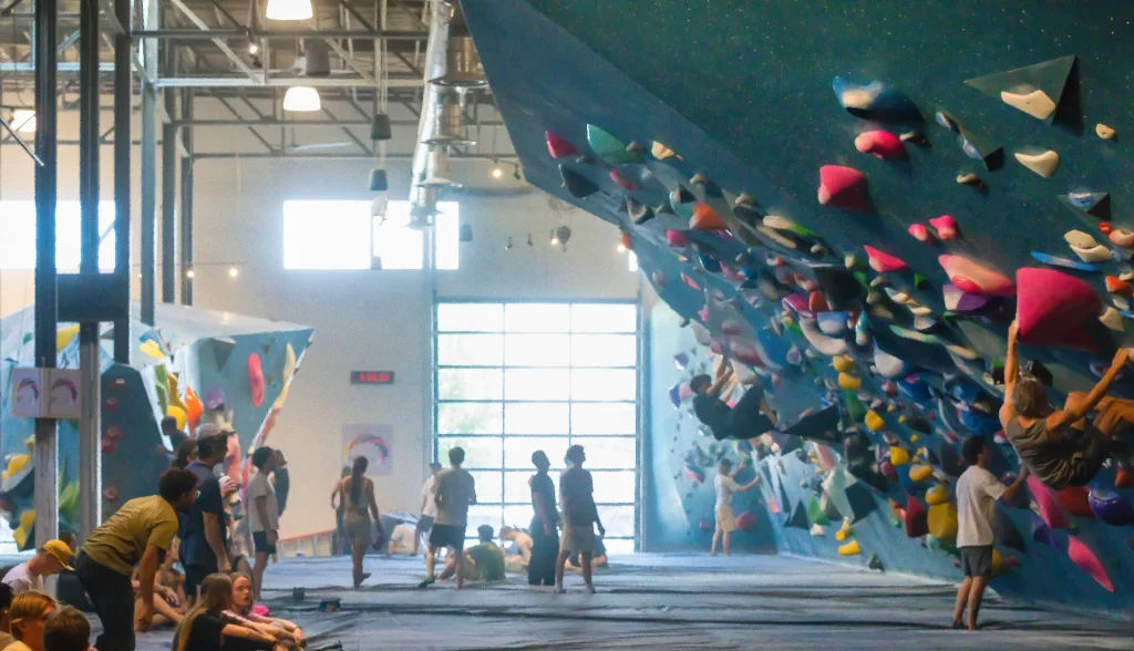Busy indoor bouldering gym with colorful climbing holds and people