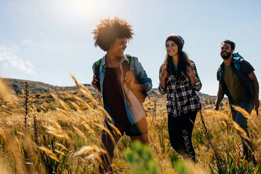 Three smiling friends hiking through sunny golden grass field