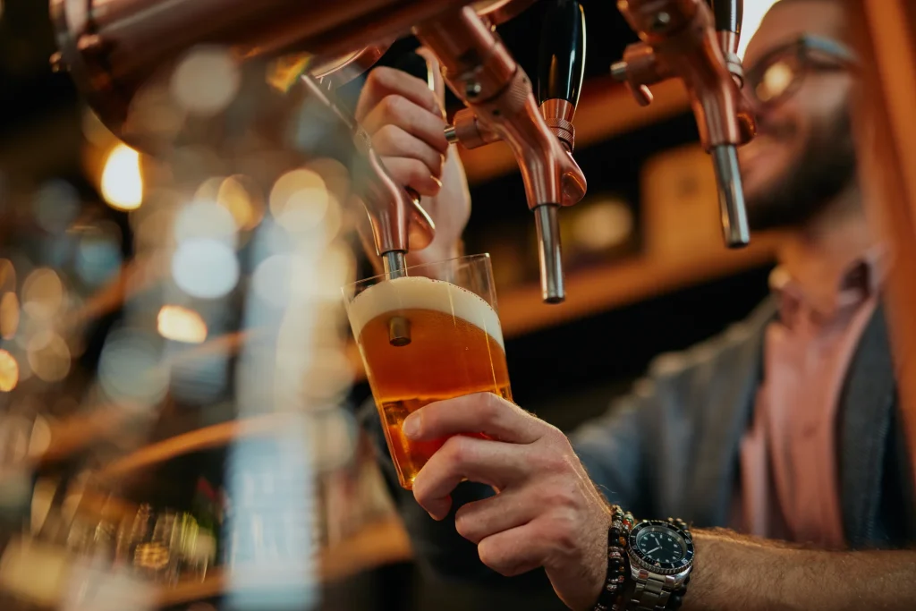 Bartender pouring draft beer from tap at bar