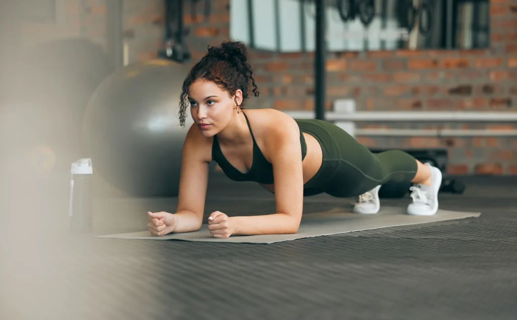 Woman in green activewear doing plank exercise on gym mat